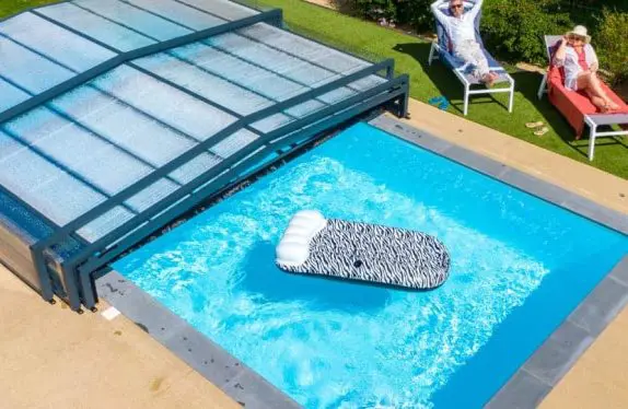Couple au bord d'une piscine couverte par un abri de piscine bas